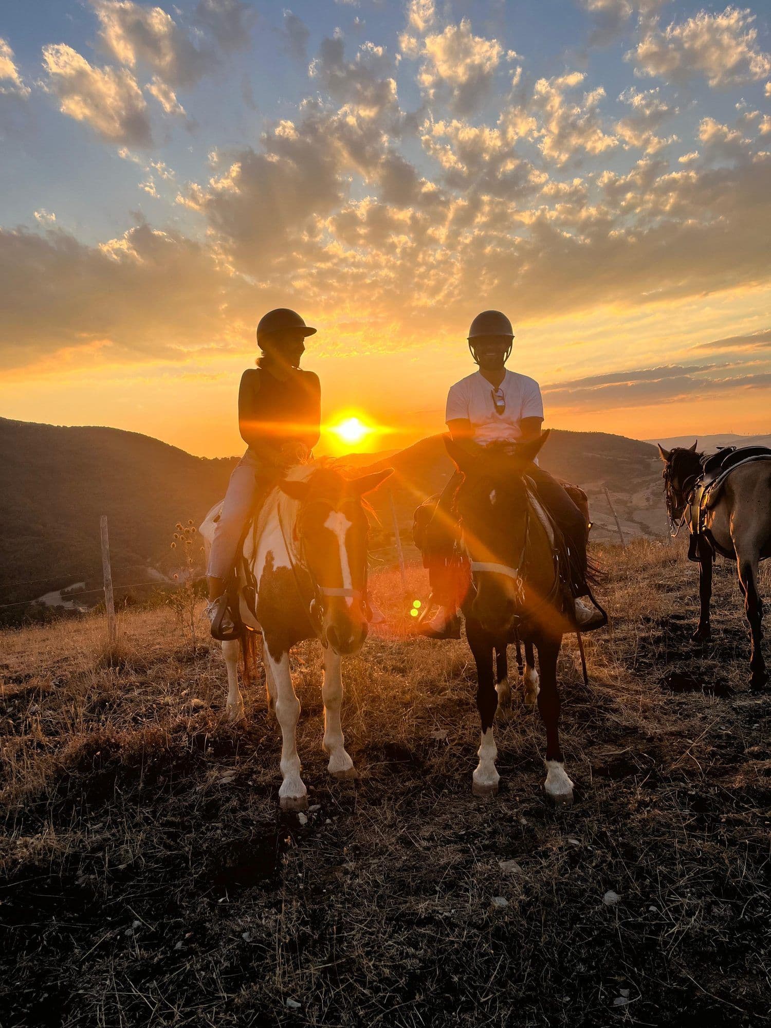 Due cavalieri in controluce al tramonto con il sole tra di loro, un terzo cavallo a destra