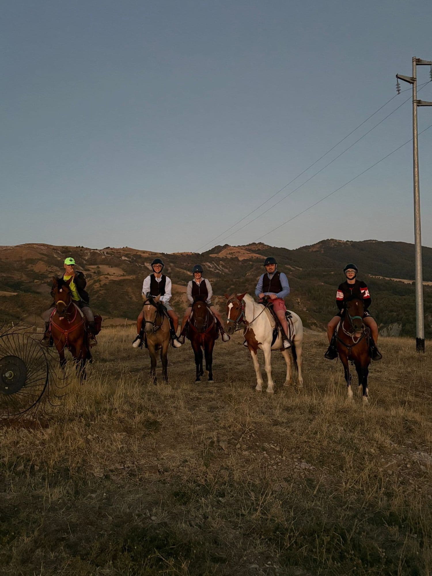 Gruppo di cinque cavalieri al tramonto guidati da un'istruttrice con cappellino fluo